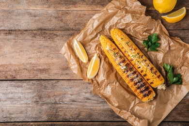 Photo of Flat lay composition of grilled corn cobs on wooden table. Space for text