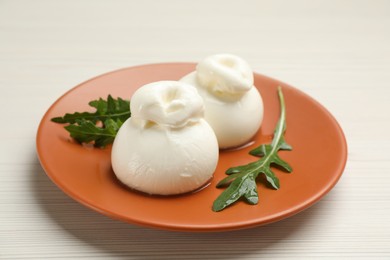 Photo of Delicious burrata cheese with arugula on white wooden table