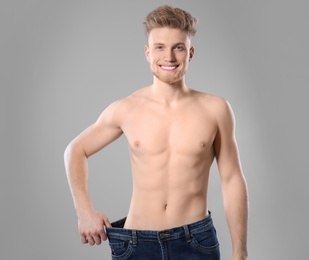 Photo of Young man with slim body in old big size jeans on grey background