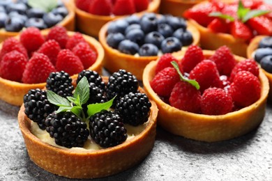 Tartlets with different fresh berries on light grey table, closeup. Delicious dessert