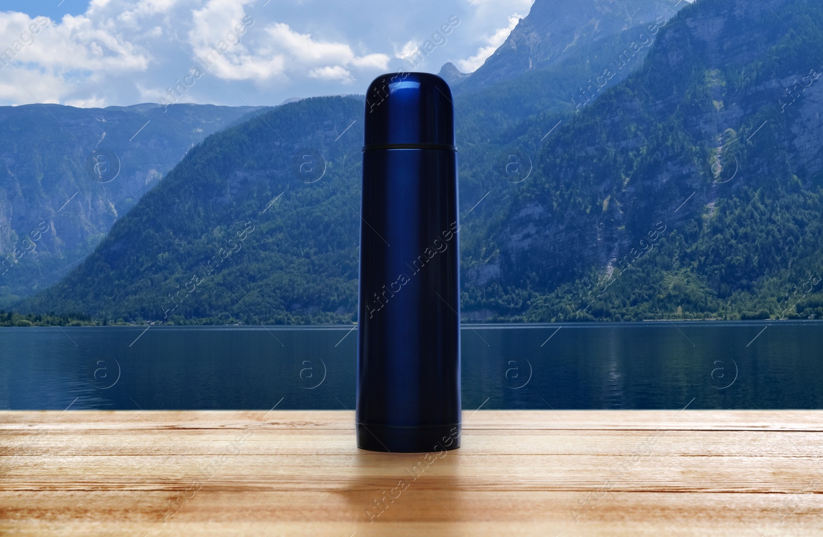 Image of Wooden desk with thermos and mountain landscape on background