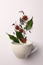 Photo of Anise stars, dry tea and green leaves falling into cup on white background, flat lay