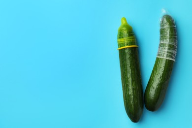 Photo of Cucumbers with condoms on light blue background, flat lay and space for text. Safe sex concept