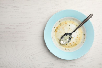 Photo of Dirty plate with food leftovers and spoon on white wooden background, top view. Space for text