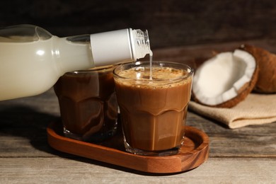 Photo of Pouring coconut syrup into glass with tasty coffee at wooden table, closeup