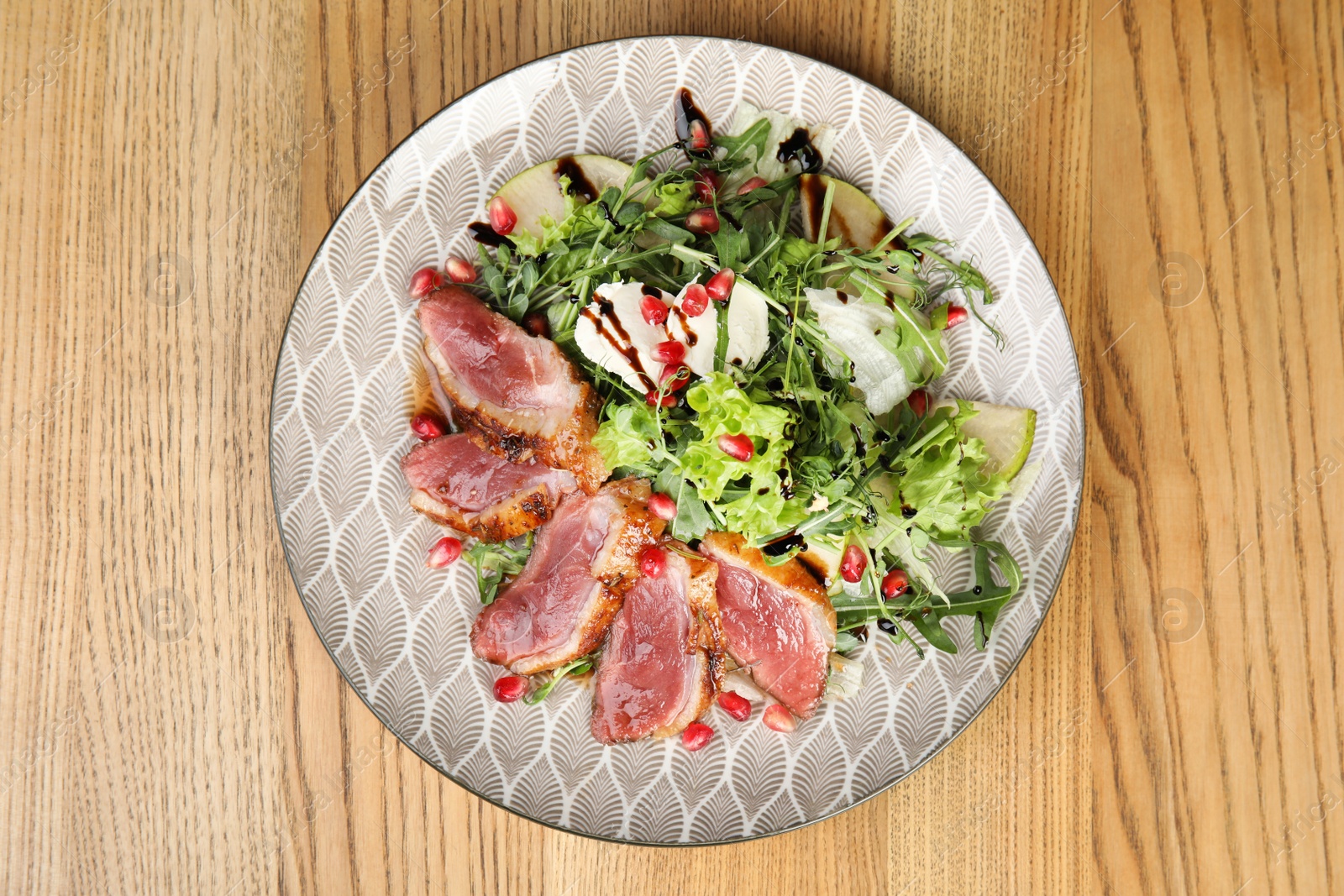 Photo of Delicious salad with roasted duck breast served on wooden table, top view