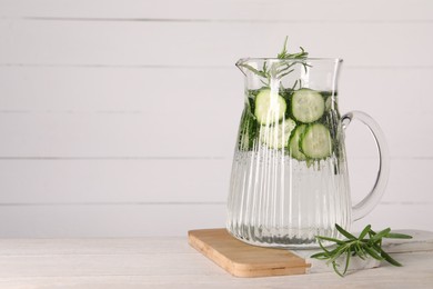 Photo of Refreshing cucumber water with rosemary in jug on light wooden table. Space for text