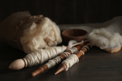 Soft white wool and spindles on wooden table, closeup