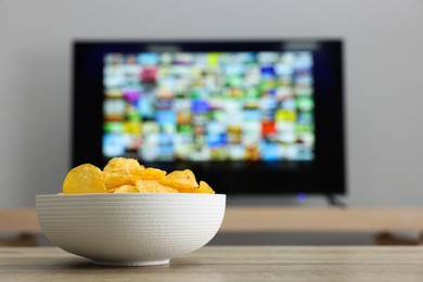 Photo of Modern TV set indoors, focus on bowl of chips