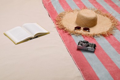Photo of Beach towel, hat, sunglasses, camera and open book on sand
