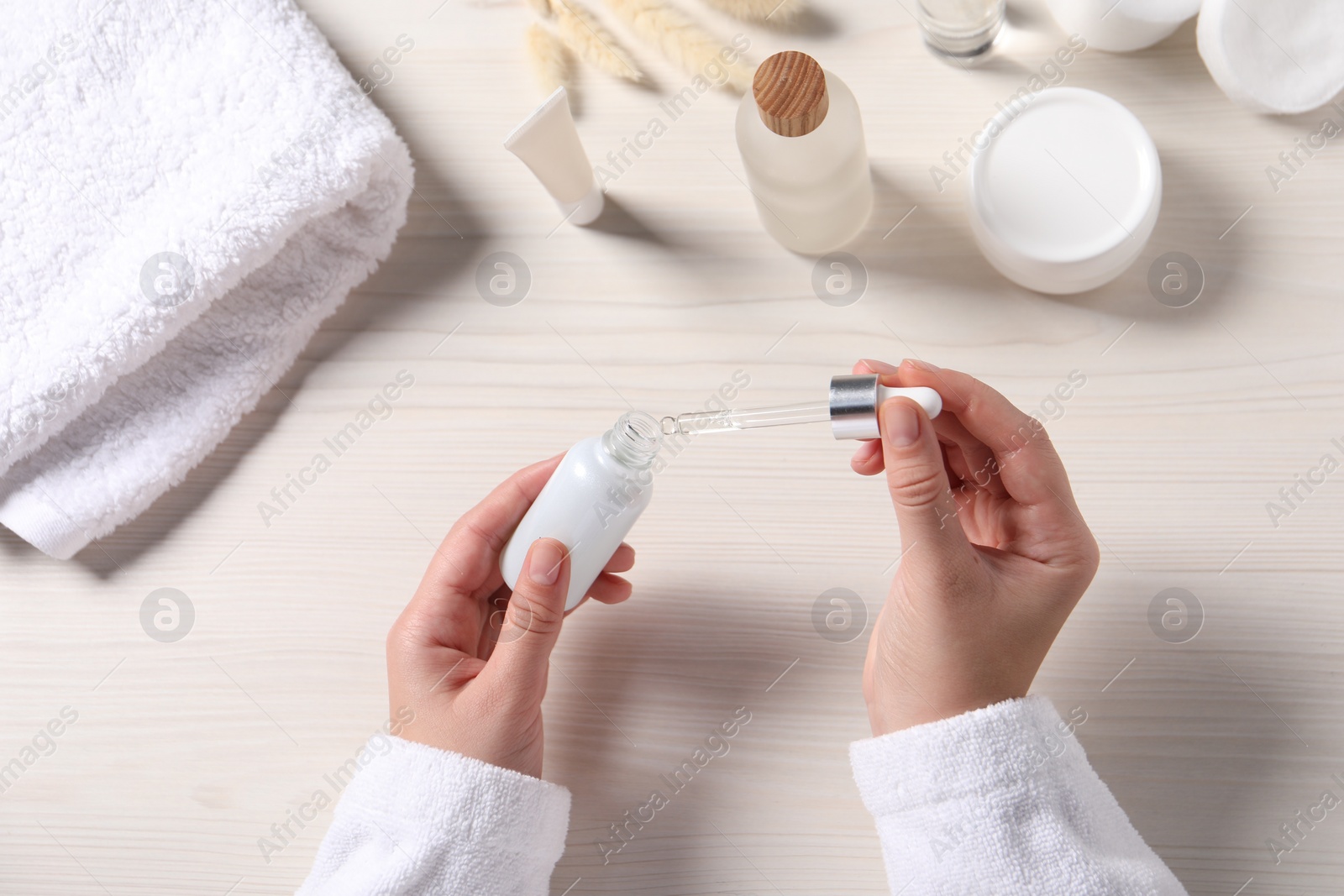 Photo of Woman with bottle and pipette of cosmetic serum at white wooden table, top view