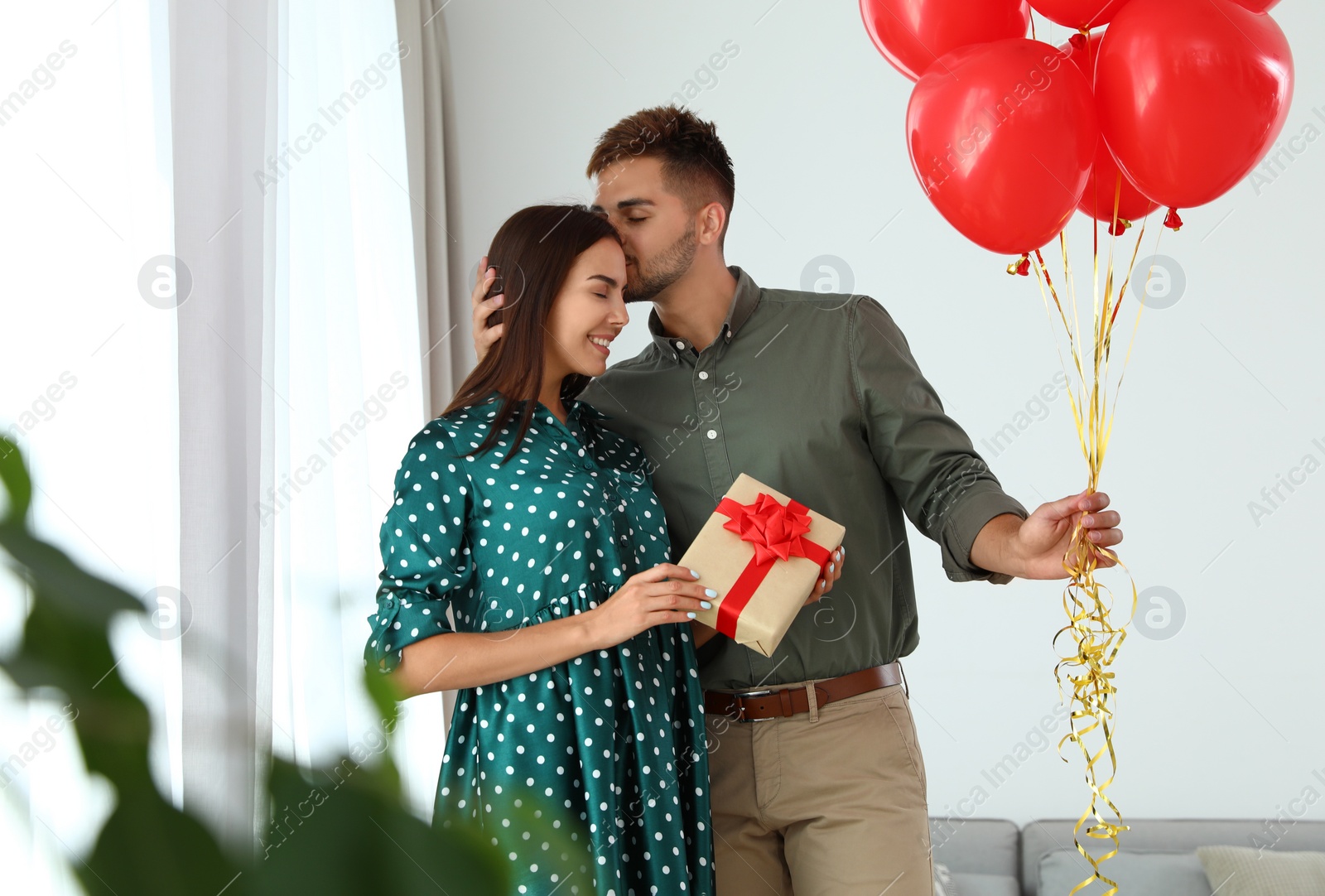 Photo of Young couple with air balloons and gift box at home. Celebration of Saint Valentine's Day