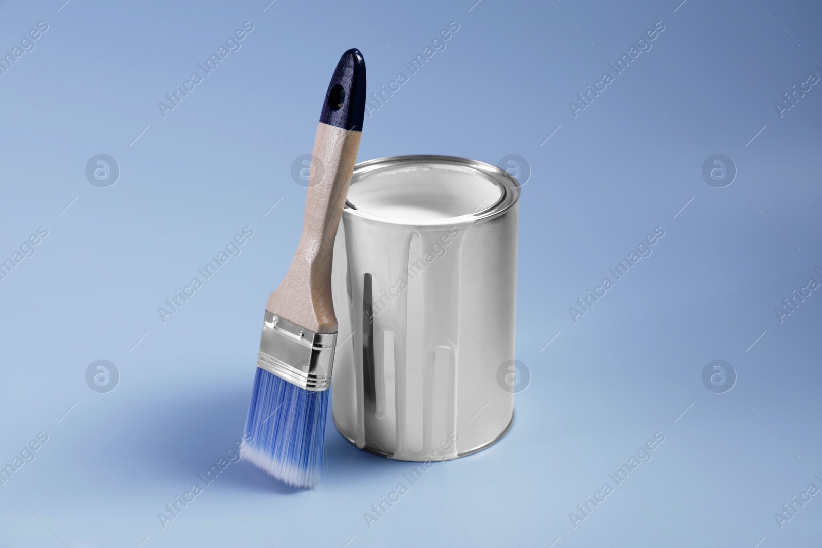 Photo of Can of white paint and brush on light blue background