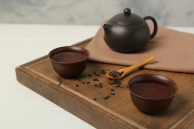 Photo of Cups of aromatic tea, dry leaves and teapot on white table