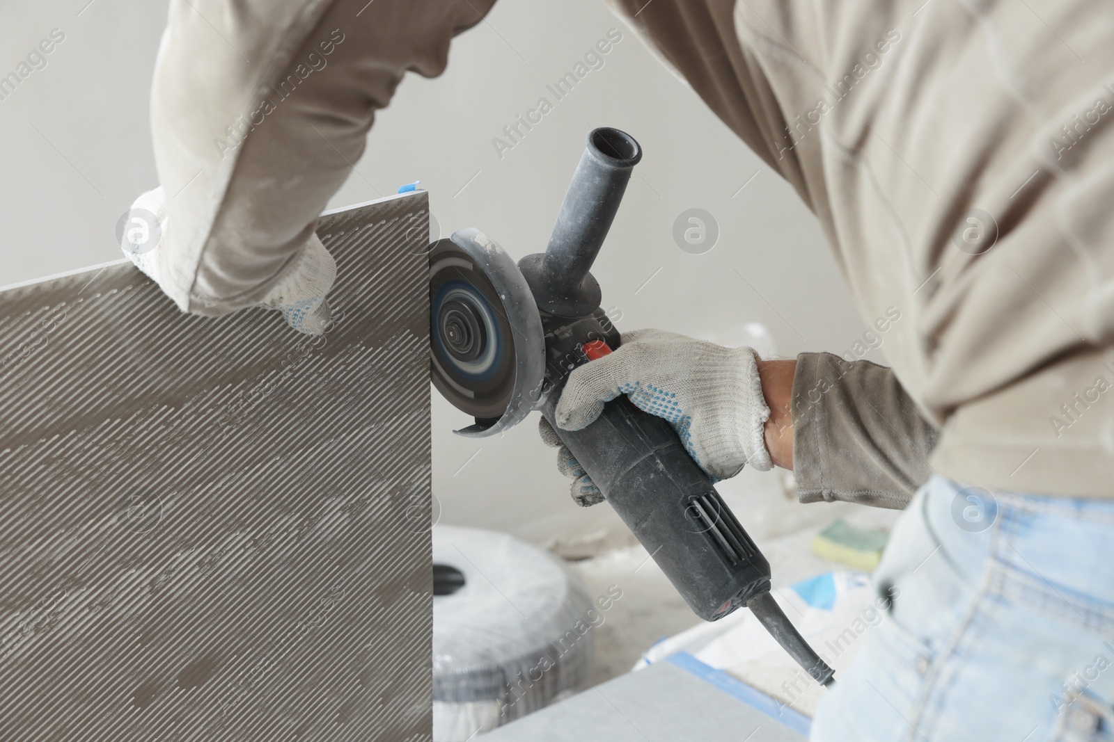 Photo of Worker cutting tile with circular saw indoors, closeup