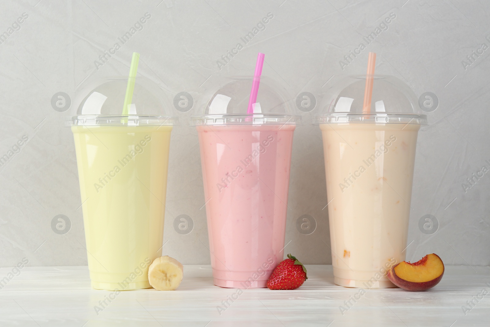 Photo of Plastic cups of different tasty smoothie and fresh fruits on white wooden table