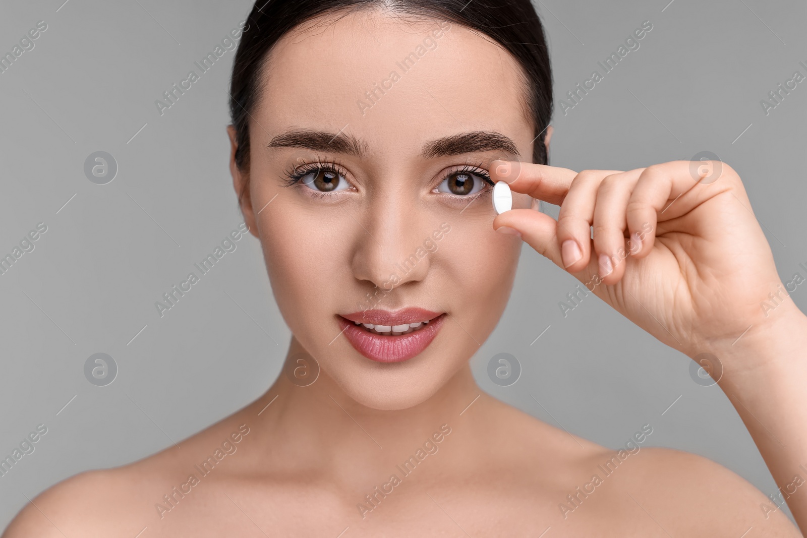 Photo of Beautiful young woman with vitamin pill on grey background