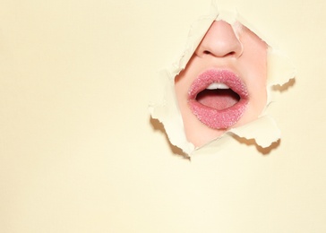 View of beautiful young woman with sugar lips through hole in color paper