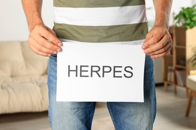 Man holding paper with word Herpes indoors, closeup