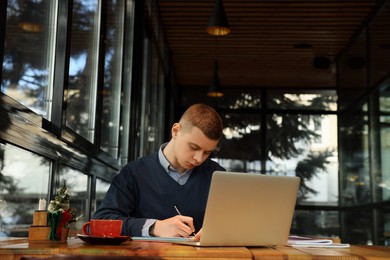 Photo of Young male student with laptop studying at table in cafe