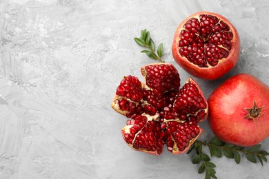 Photo of Fresh pomegranates and green leaves on grey textured table, flat lay. Space for text
