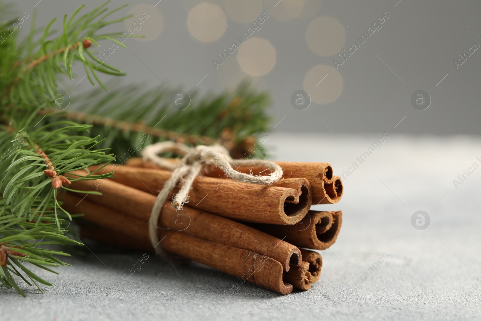 Photo of Bunch of cinnamon sticks and fir branches on grey textured table, closeup. Space for text