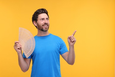 Photo of Happy man holding hand fan on orange background. Space for text