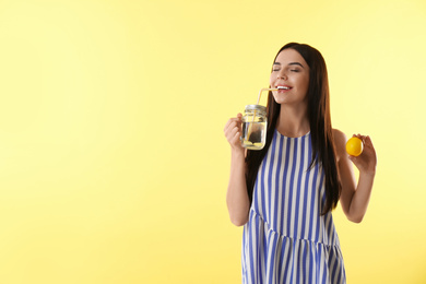 Photo of Beautiful young woman with fresh fruit drinking tasty lemon water on yellow background. Space for text