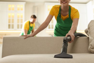 Photo of Professional janitor in uniform vacuuming sofa indoors, closeup. Space for text
