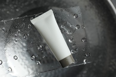 Photo of Moisturizing cream in tube on glass with water drops against metal background, top view