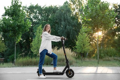 Photo of Happy woman with modern electric kick scooter in park