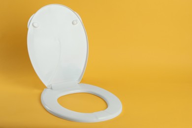 Photo of New white plastic toilet seat on yellow background, space for text