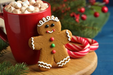 Photo of Tasty gingerbread man cookie and cocoa with marshmallows on blue wooden table, closeup