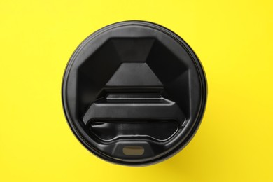 One paper cup with black lid on yellow background, top view. Coffee to go