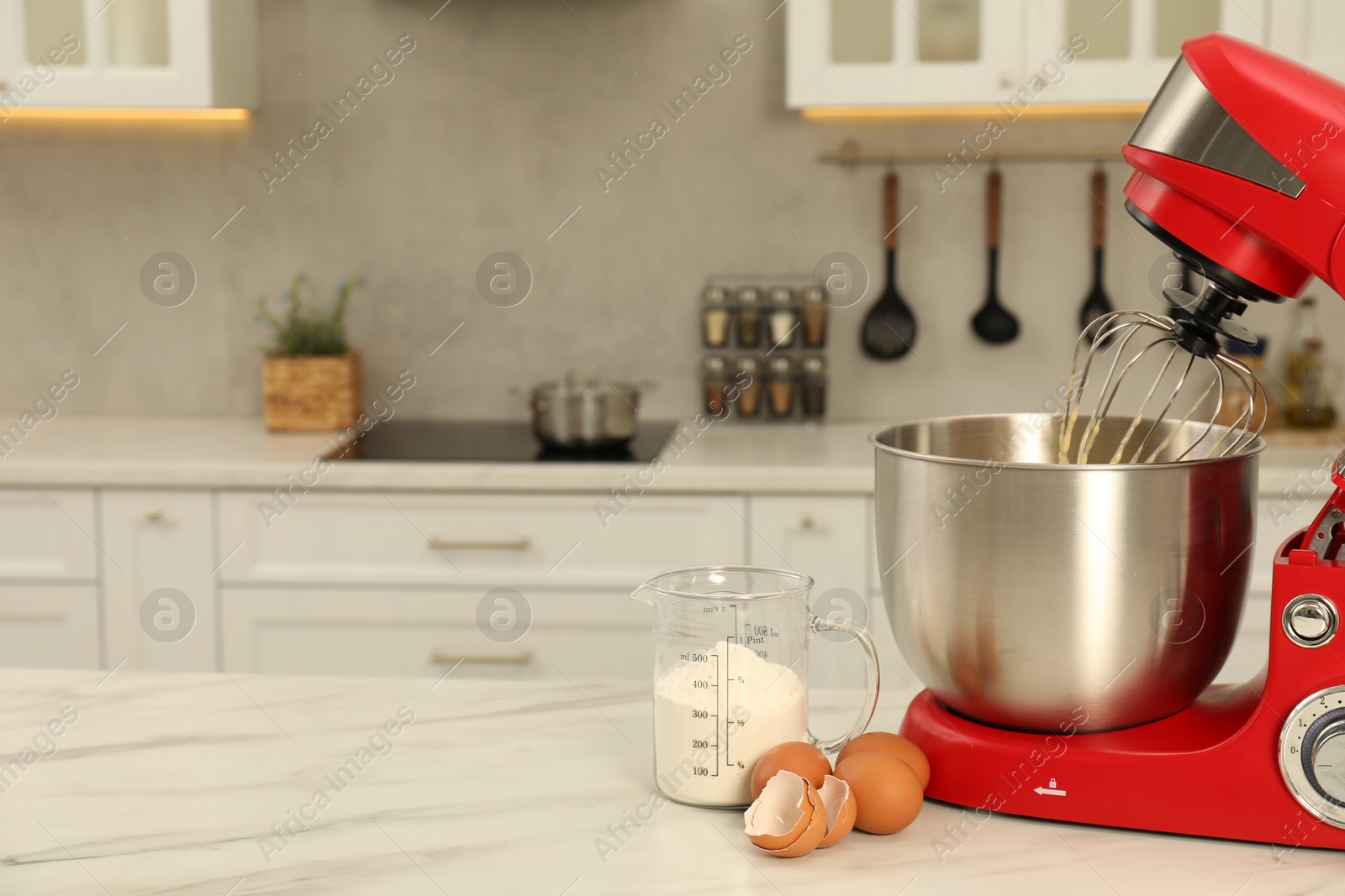 Photo of Modern red stand mixer, eggs and container with flour on white marble table in kitchen, space for text