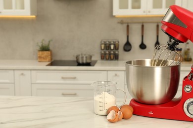 Photo of Modern red stand mixer, eggs and container with flour on white marble table in kitchen, space for text