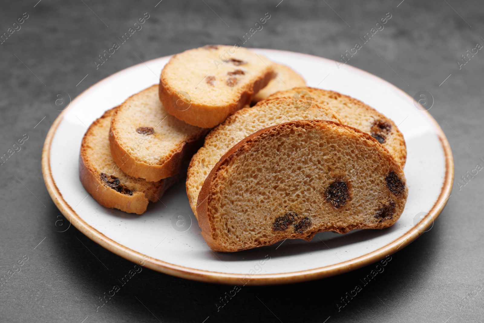 Photo of Plate of sweet hard chuck crackers with raisins on grey table, closeup