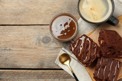 Photo of Delicious chocolate brownies with nuts and caramel sauce on wooden table, flat lay. Space for text