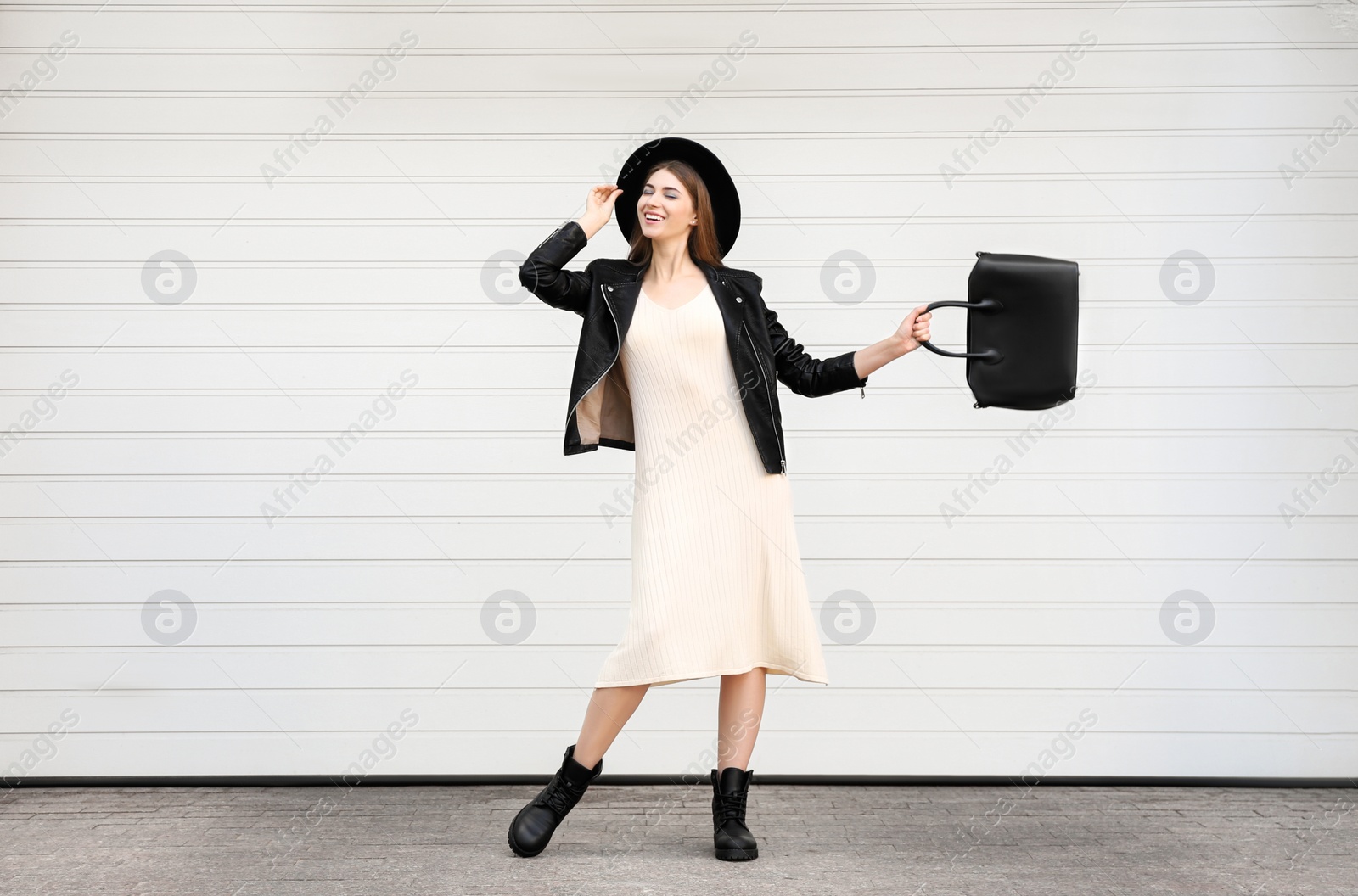 Photo of Beautiful young woman with stylish leather bag near white wall outdoors
