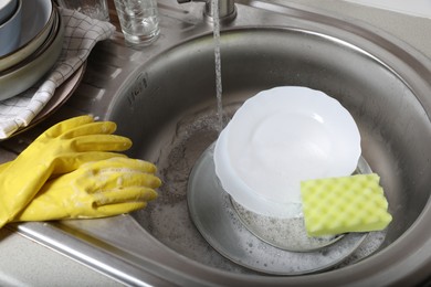 Photo of Washing plates, sponge and rubber gloves in kitchen sink