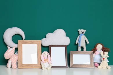 Photo of Soft toys and photo frames on table against green background, space for text. Child room interior