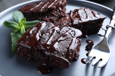 Photo of Delicious chocolate brownies with sweet syrup and mint on plate, closeup