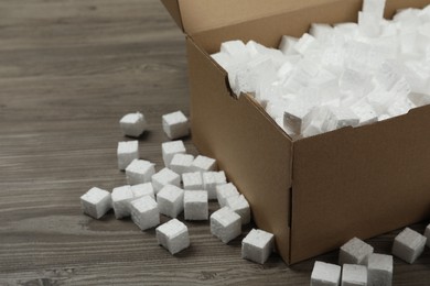 Photo of Cardboard box and styrofoam cubes on wooden floor, closeup