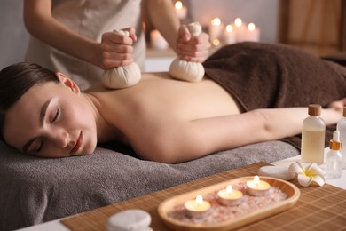 Photo of Spa therapy. Beautiful young woman lying on table during herbal bag massage in salon