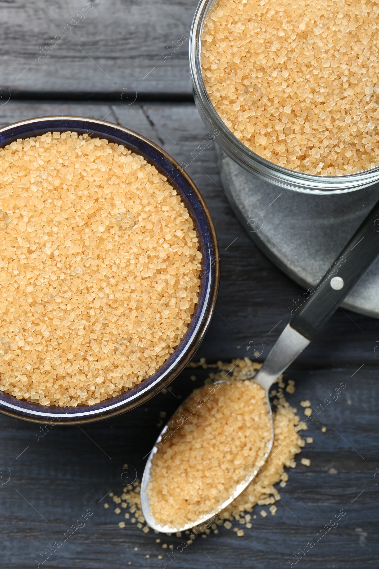Brown sugar in bowls and spoon on black wooden table, flat lay Photo of Brown sugar in bowls and spoon on black wooden table, flat lay