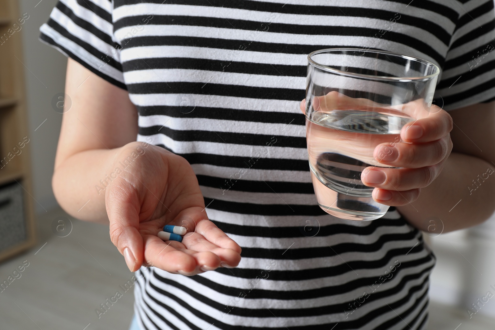 Photo of Woman with glass of water and pills on blurred background, closeup
