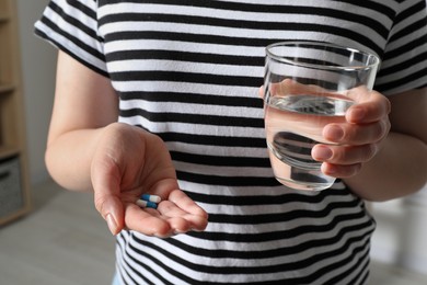 Photo of Woman with glass of water and pills on blurred background, closeup