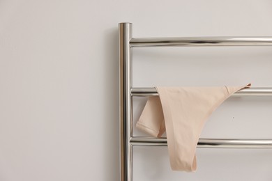 Photo of Heated towel rail with beige underwear on white wall, closeup. Space for text