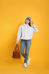Photo of Beautiful young woman with stylish leather backpack and headphones on yellow background
