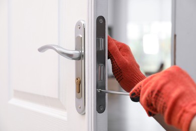 Photo of Handyman with screwdriver repairing door lock indoors, closeup